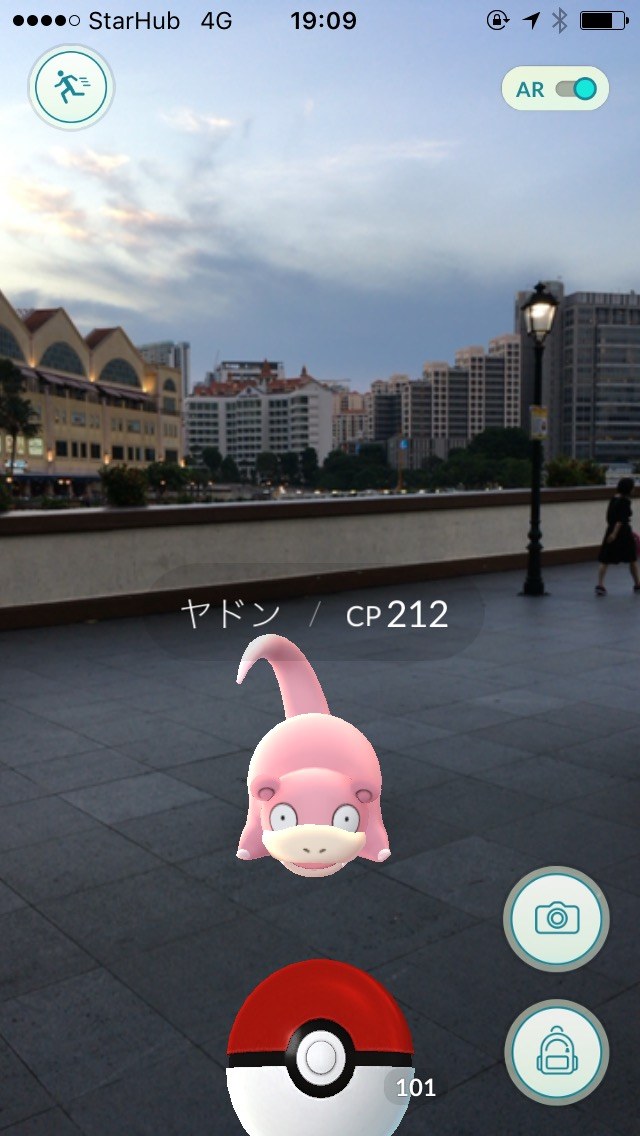 ポケモン GO の AR 画面。川沿いの遊歩道にヤドン（CP212）が現れている。夕暮れの空と対岸の建物