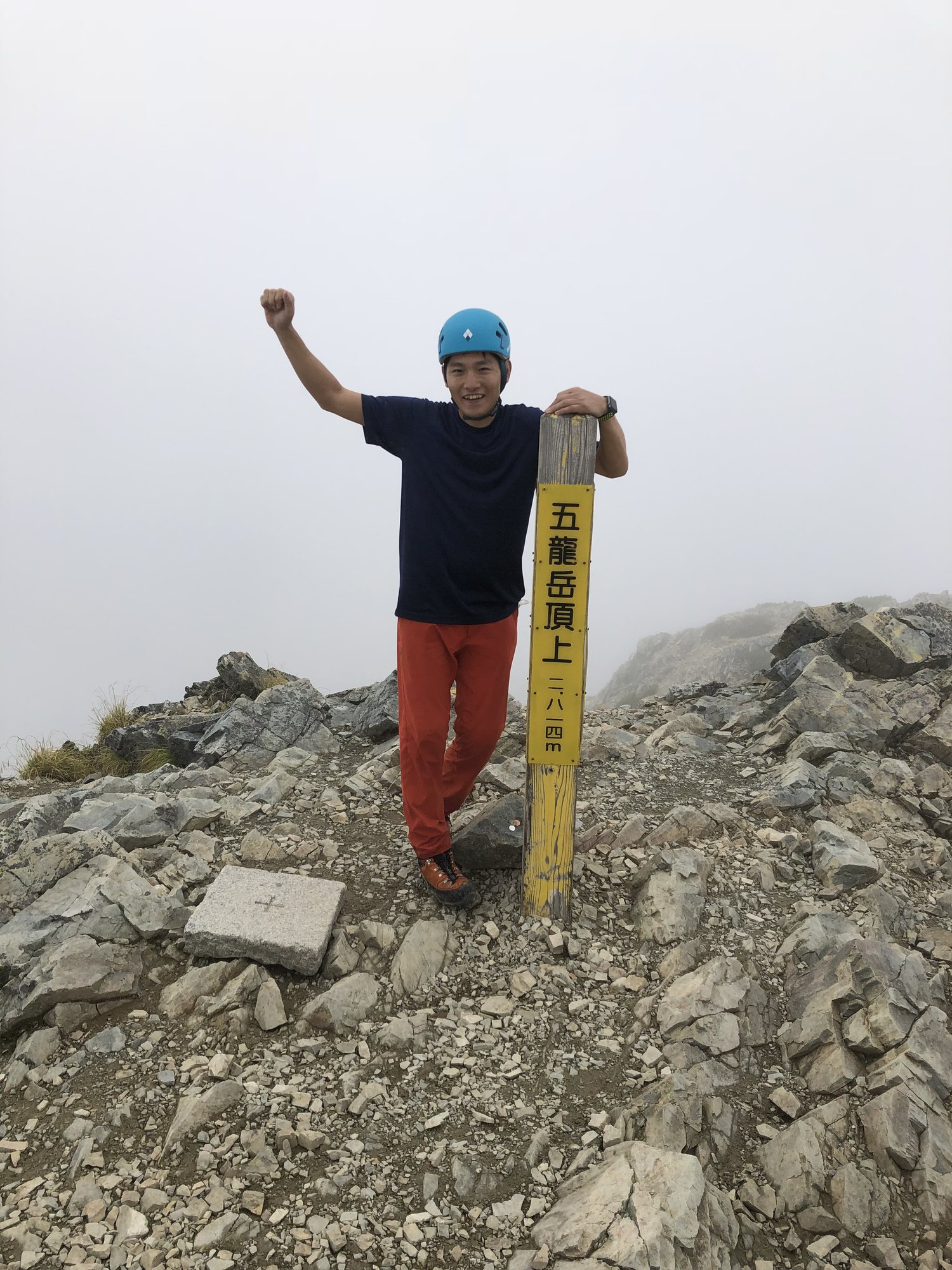 五竜岳頂上(2,814m)の標柱の横で、ヘルメット姿でこぶしを上げる自分