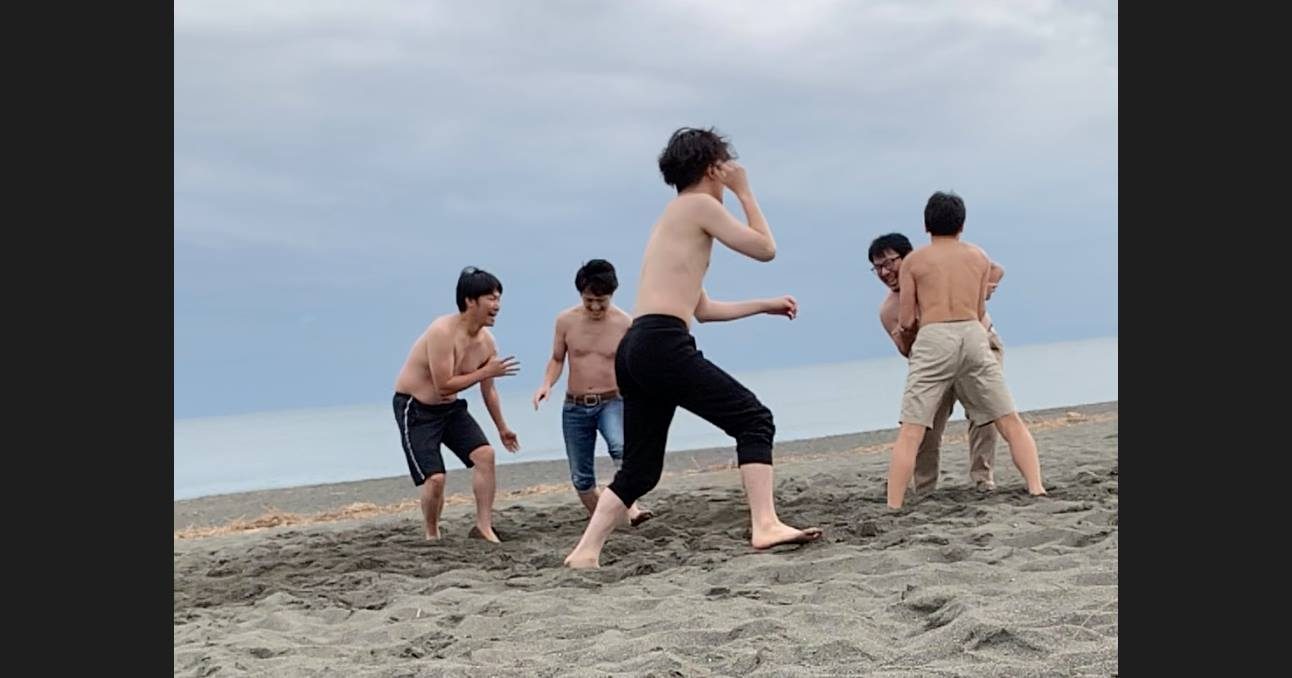 砂浜での相撲バトル。一人が身構え、奥では2人が組み合っている