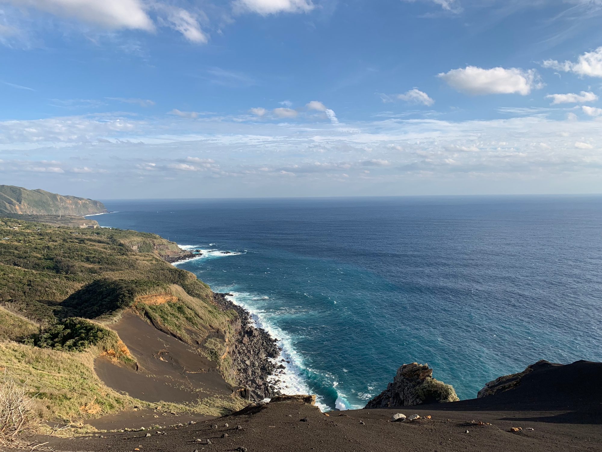 黒い火山性の斜面から見下ろした海岸線。断崖と濃紺の海が奥まで続く
