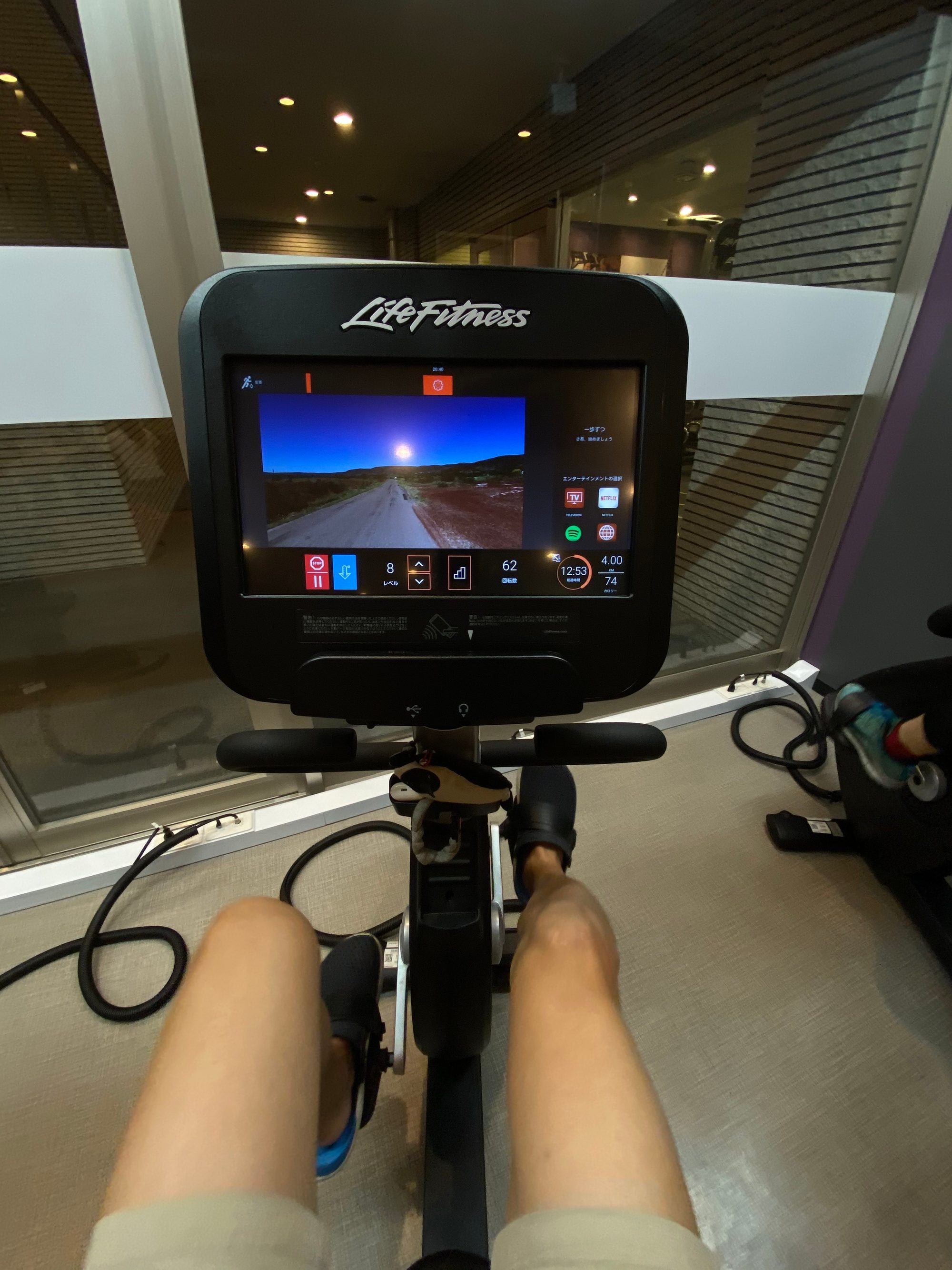 ジムのエアロバイク。Life Fitness のモニターに走行動画や Netflix・Spotify のアイコンが並ぶ