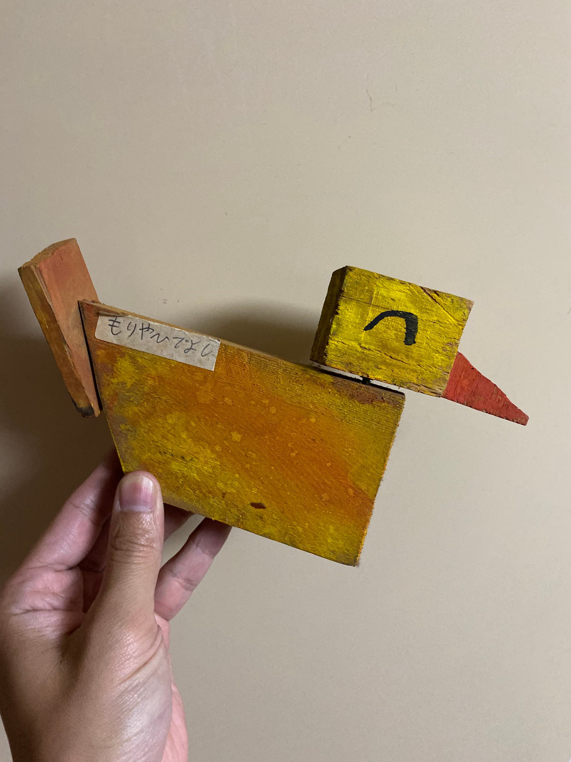 子どもの頃に図工で作った、黄色く塗った木の鳥のオブジェ（赤いとさか付き）を手に持っている
