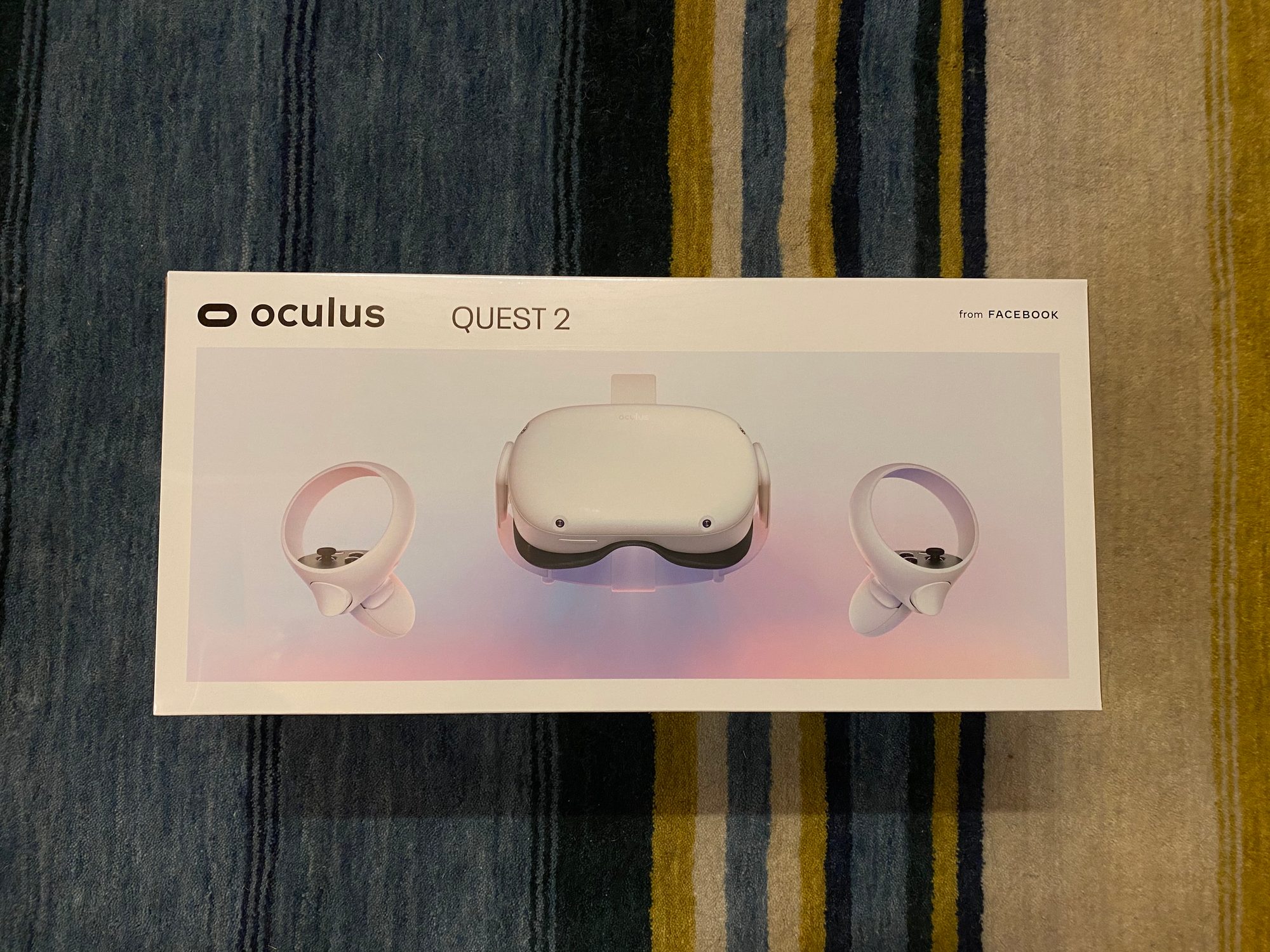 床のラグに置かれた Oculus Quest 2 の箱（from FACEBOOK）。ヘッドセットと2本のコントローラーが印刷されている