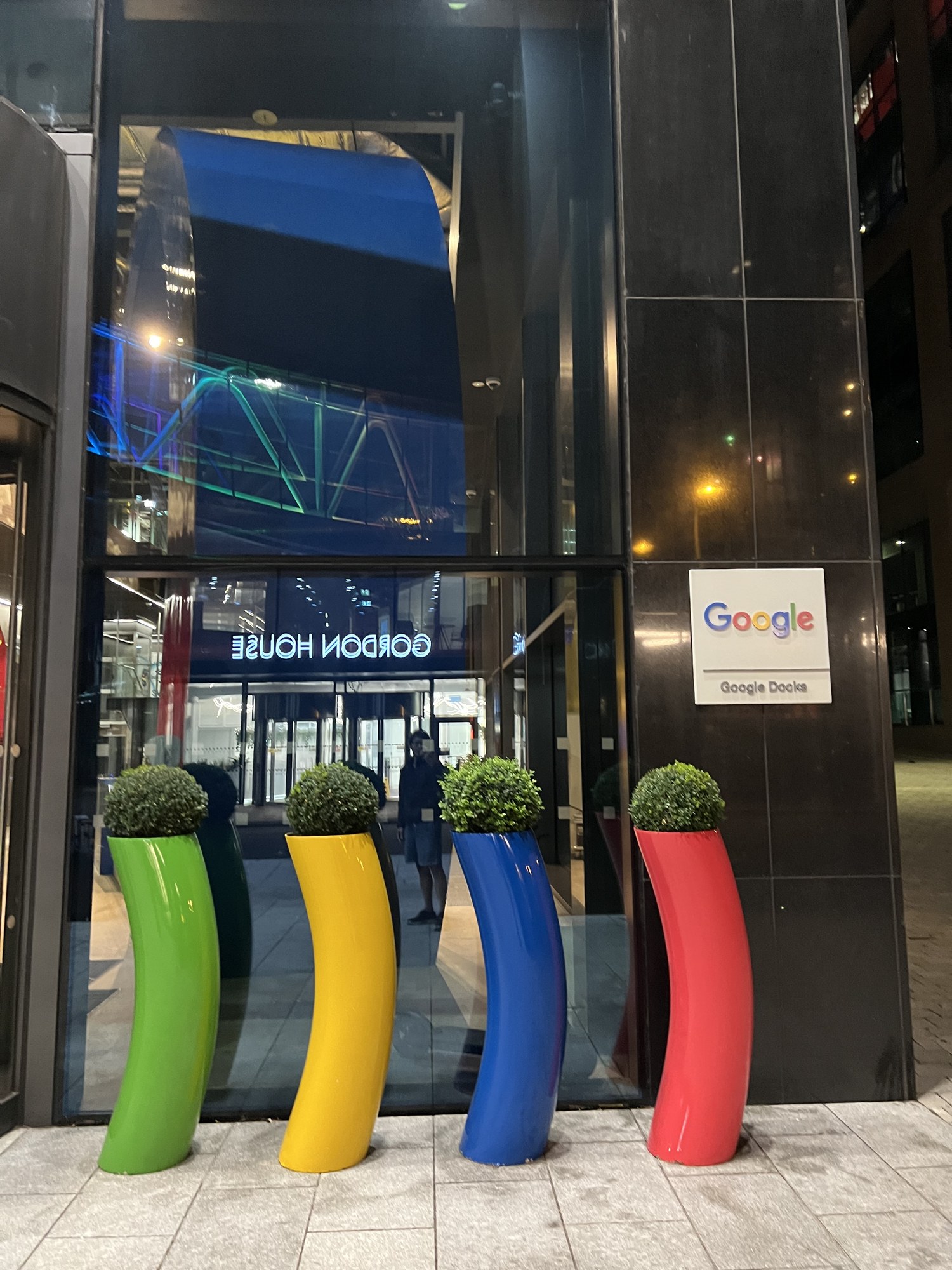 Google Docks（Gordon House）の入口。Google のロゴの看板と、緑・黄・青・赤の曲がった植木鉢が並ぶ