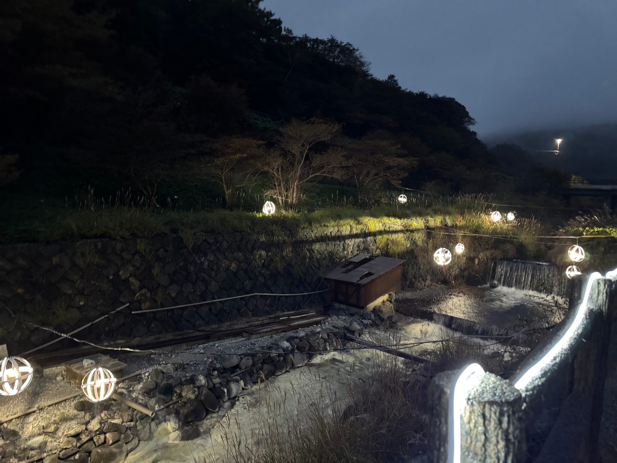 夜の那須・鹿の湯周辺。川沿いに球体のイルミネーションが灯り、湯気の立つ温泉地