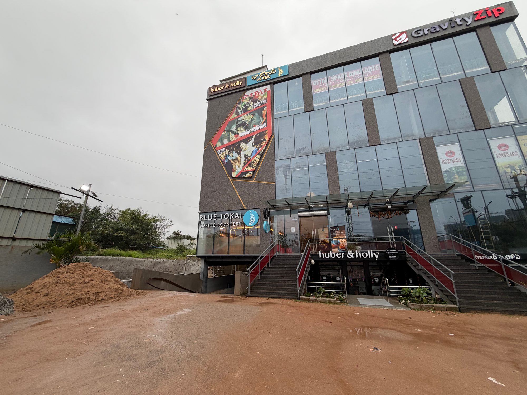 Blue Tokai Coffee Roasters が入る Hyderabad のビル外観。赤土の地面と曇り空、GravityZip の看板