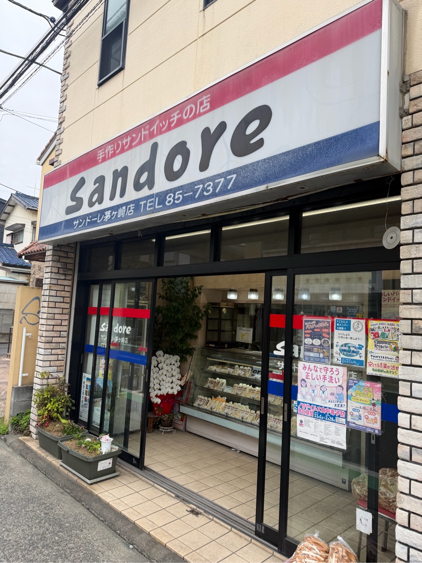 サンドーレ茅ヶ崎店の店構え。赤と青のラインが入った Sandore の看板「手作りサンドイッチの店」、ガラス越しにサンドイッチが並ぶショーケース