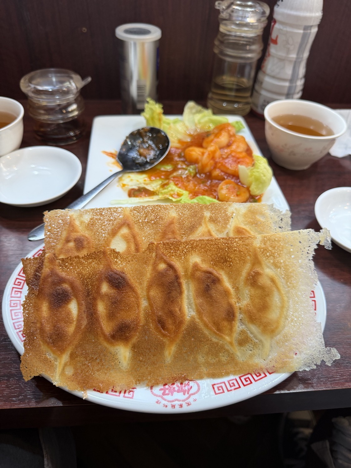ニーハオ蒲田店の羽根付きギョーザ。手前の白い皿に5個のギョーザが並び、一枚の大きなレース状の薄い羽根がまるごと覆っている。奥にはエビチリ、両脇に烏龍茶の入った小さな茶碗